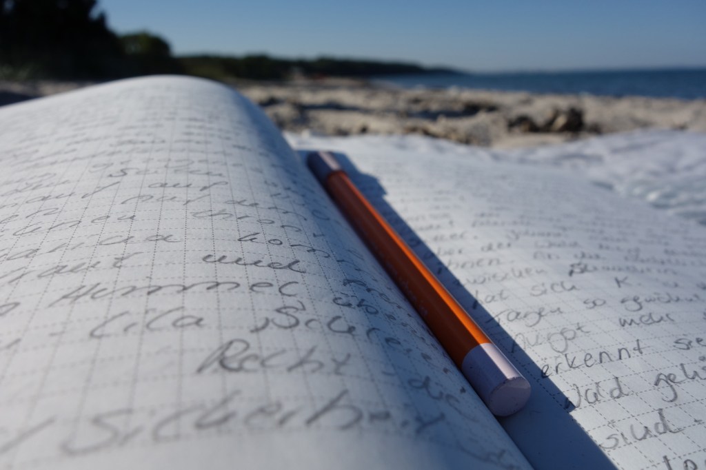 Notizbuch und Bleistift am Strand,
