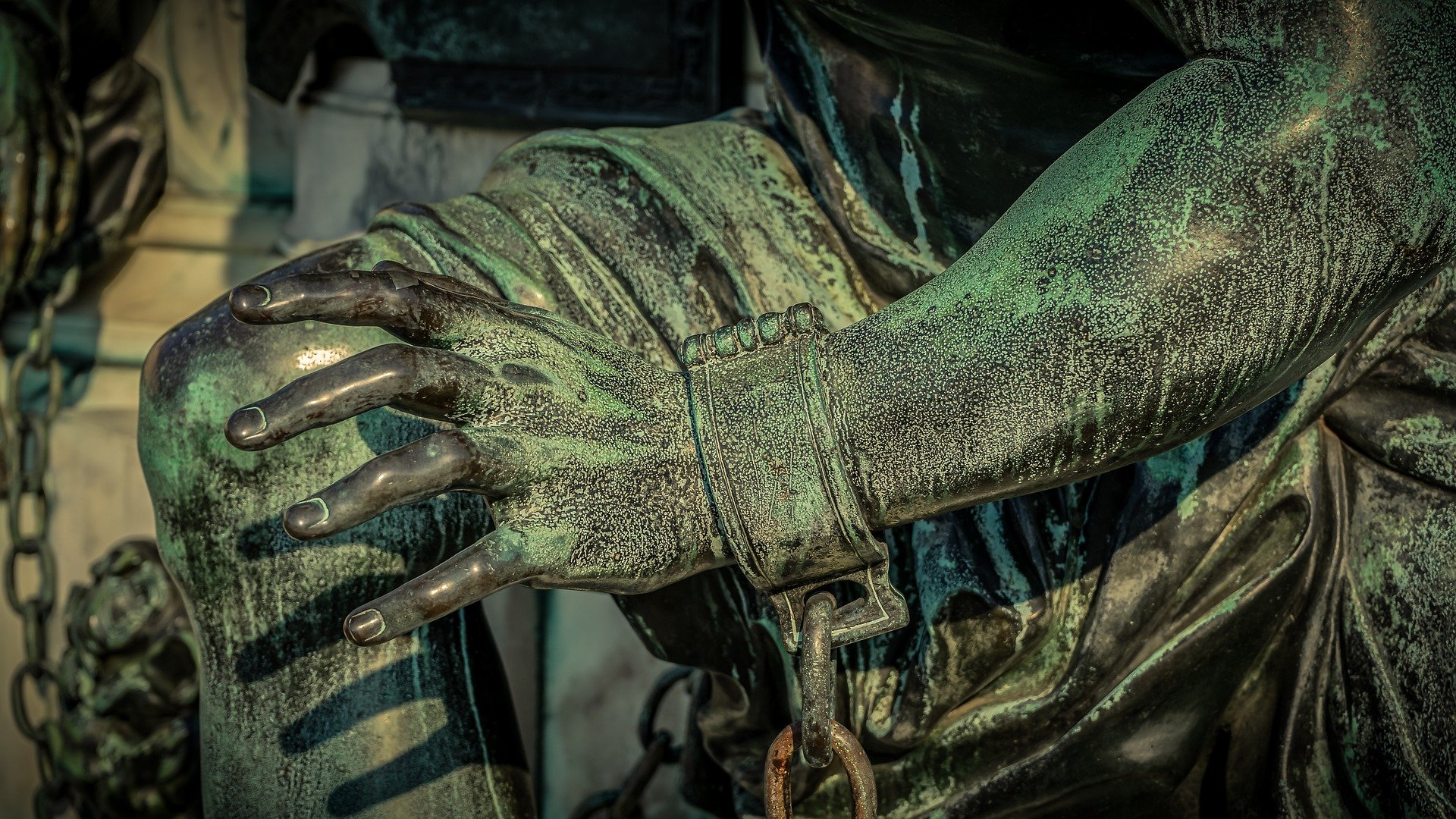 Detail einer Statue, das deren Hand mit Fessel und Eisenkette zeigt.
