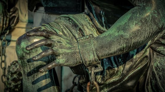 Detail einer Statue, das deren Hand mit Fessel und Eisenkette zeigt.