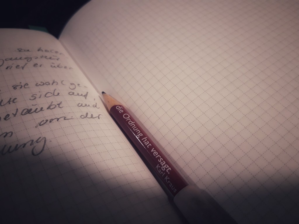 Aufgeschlagenes Notizbuch, darauf ein Bleistift, auf dem steht: die Ordnung hat versagt. Karl Kraus