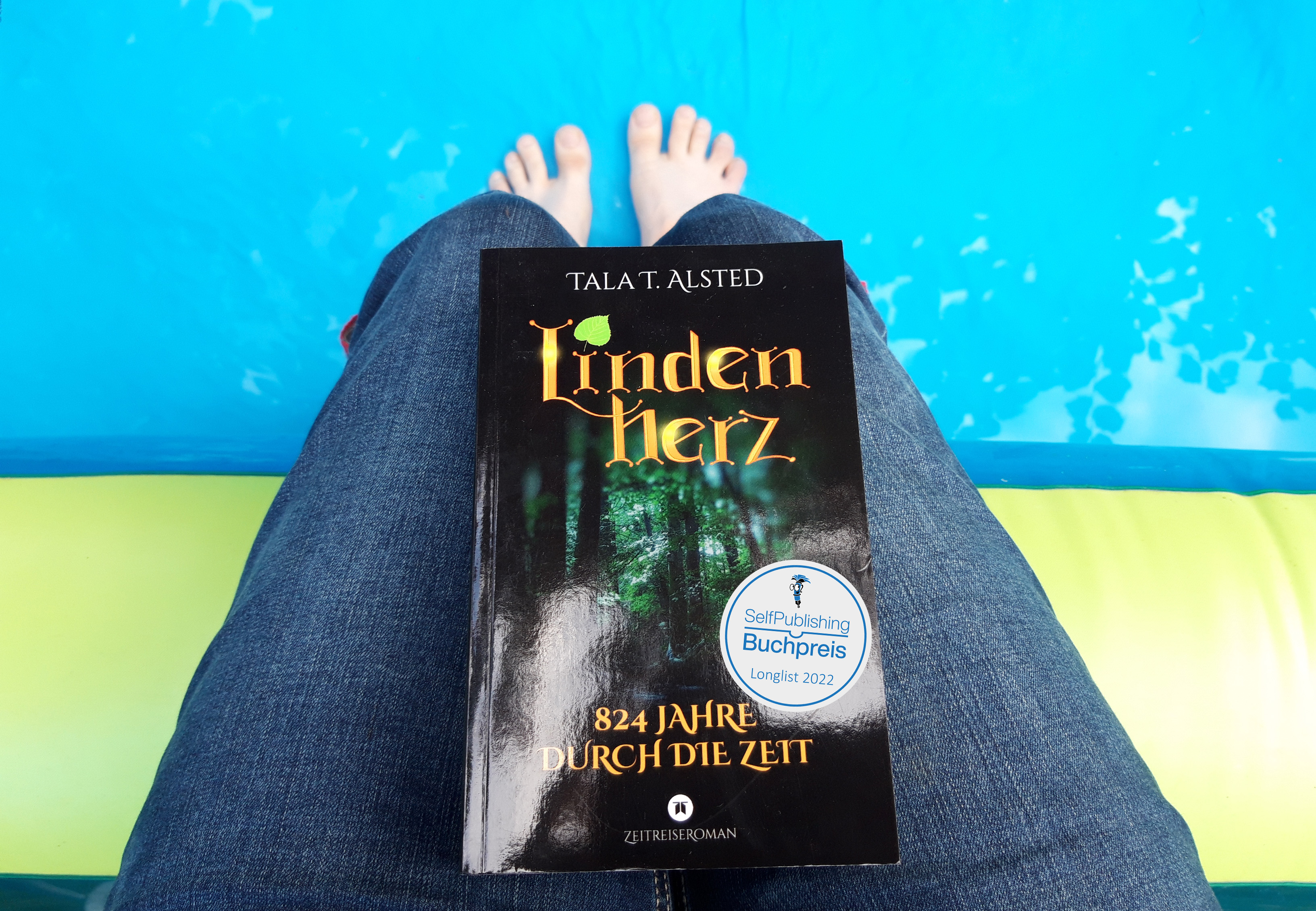 Buch "Lindenherz - 824 Jahre durch die Zeit" von Tala T. Alsted auf dem Schoß, dazu der Longlist-Batch des SelfPublishing Buchpreis