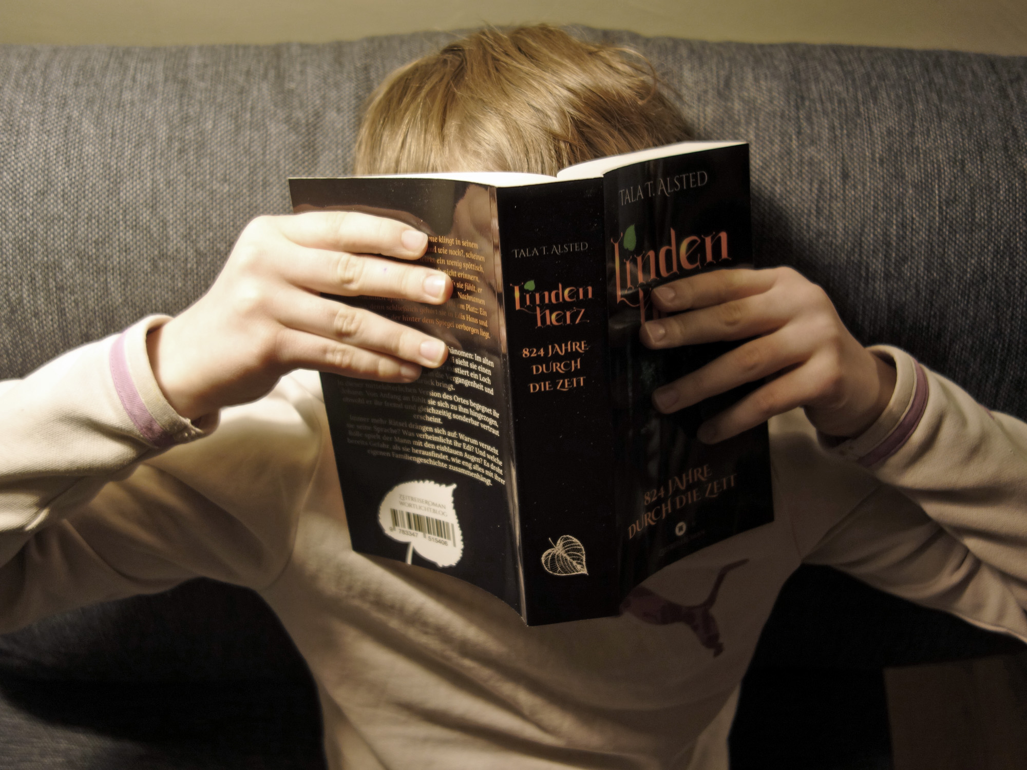 Jemand liest das Buch "Lindenherz - 824 Jahre durch die Zeit" von Tala T. Alsted - man sieht die Hände, den Buchrücken und ein Stück des Kopfes