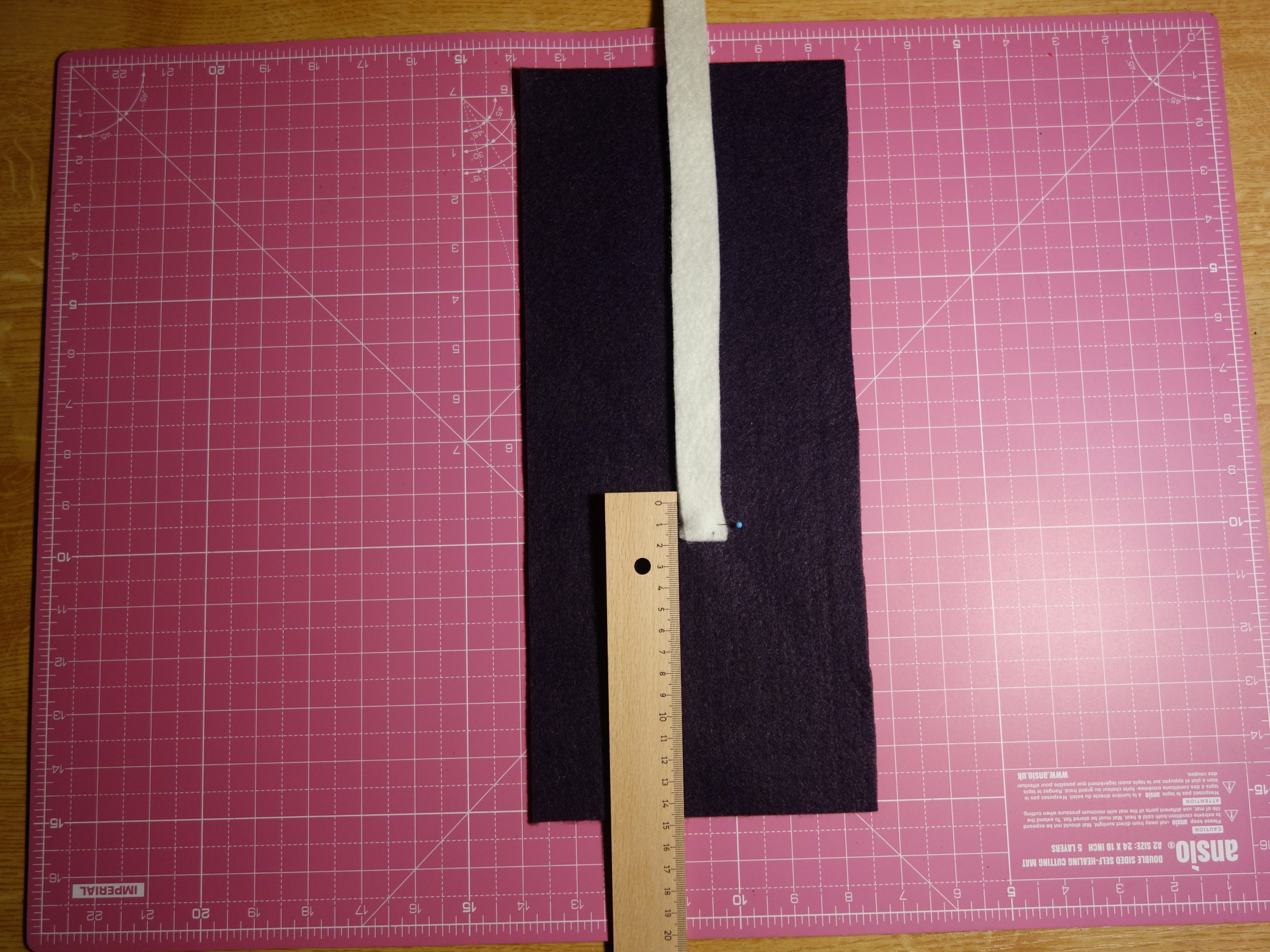 Das dünne Verschlussband ist auf dem violetten Rechteck mit einer Stecknadel festgesteckt - in Höhe von etwa 14 Zentimetern vom Rand