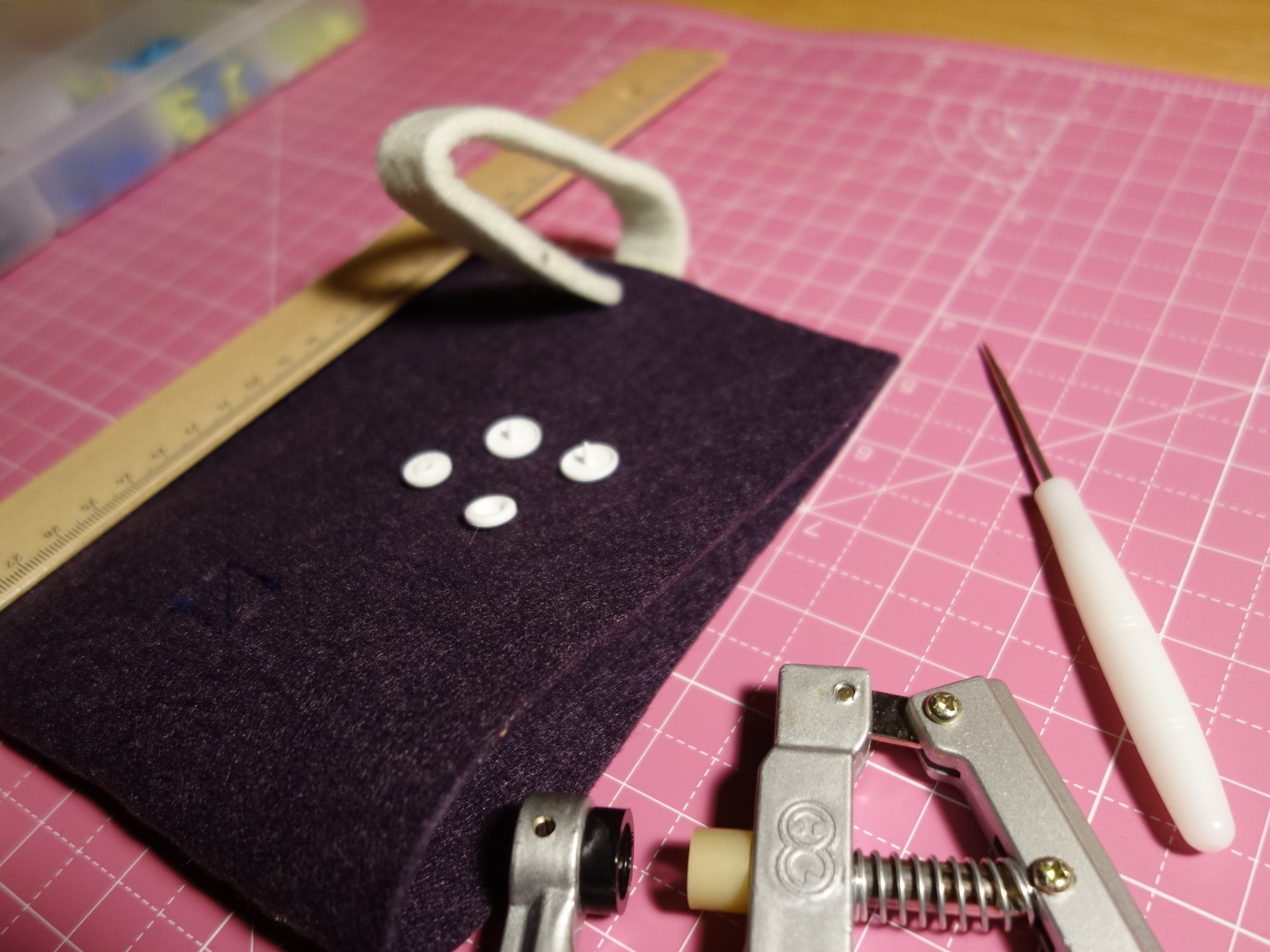 Bevor die E-Book-Reader-Hülle zusammengenäht wird, sollten als Verschluss ein Druckknopf oder ein Klettverschluss angebracht werden. Auf dem Bild liegt ein weißer Plastikdruckknopf bereit.