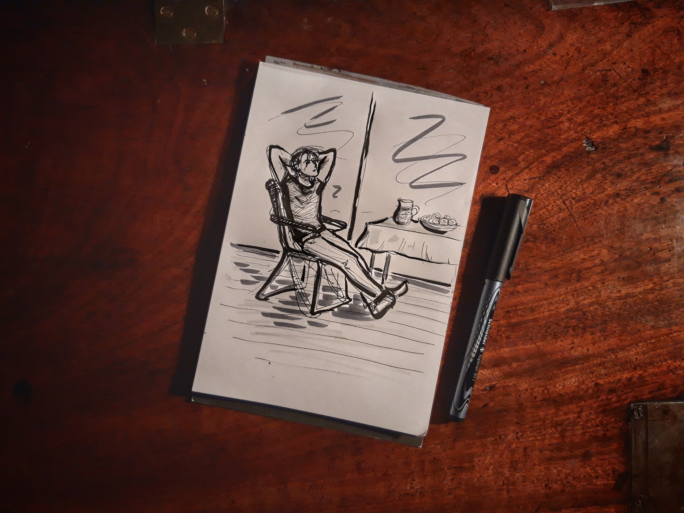 Zeichenblock und Stift, eine Schwarz-Weiß-Zeichnung von einem jungen Mann auf einem Klappstuhl mit hinter dem Kopf verschränkten Armen