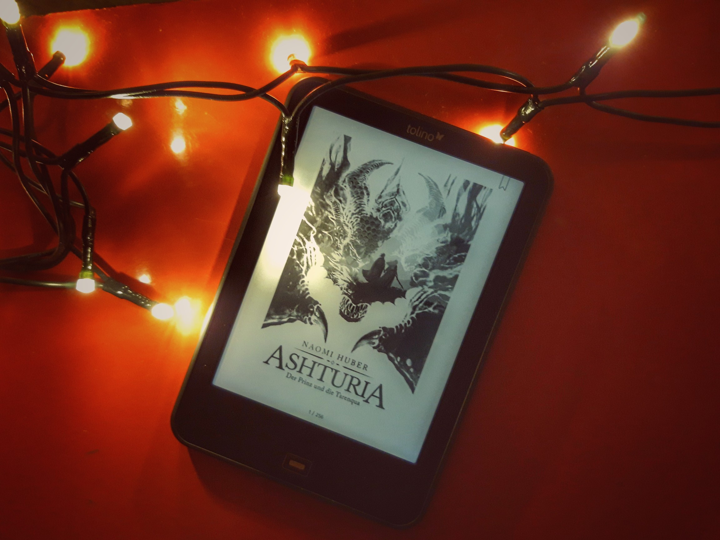 E-Book-Reader mit dem Cover von "Ashturia" von Naomi Huber, daneben eine Lichterkette