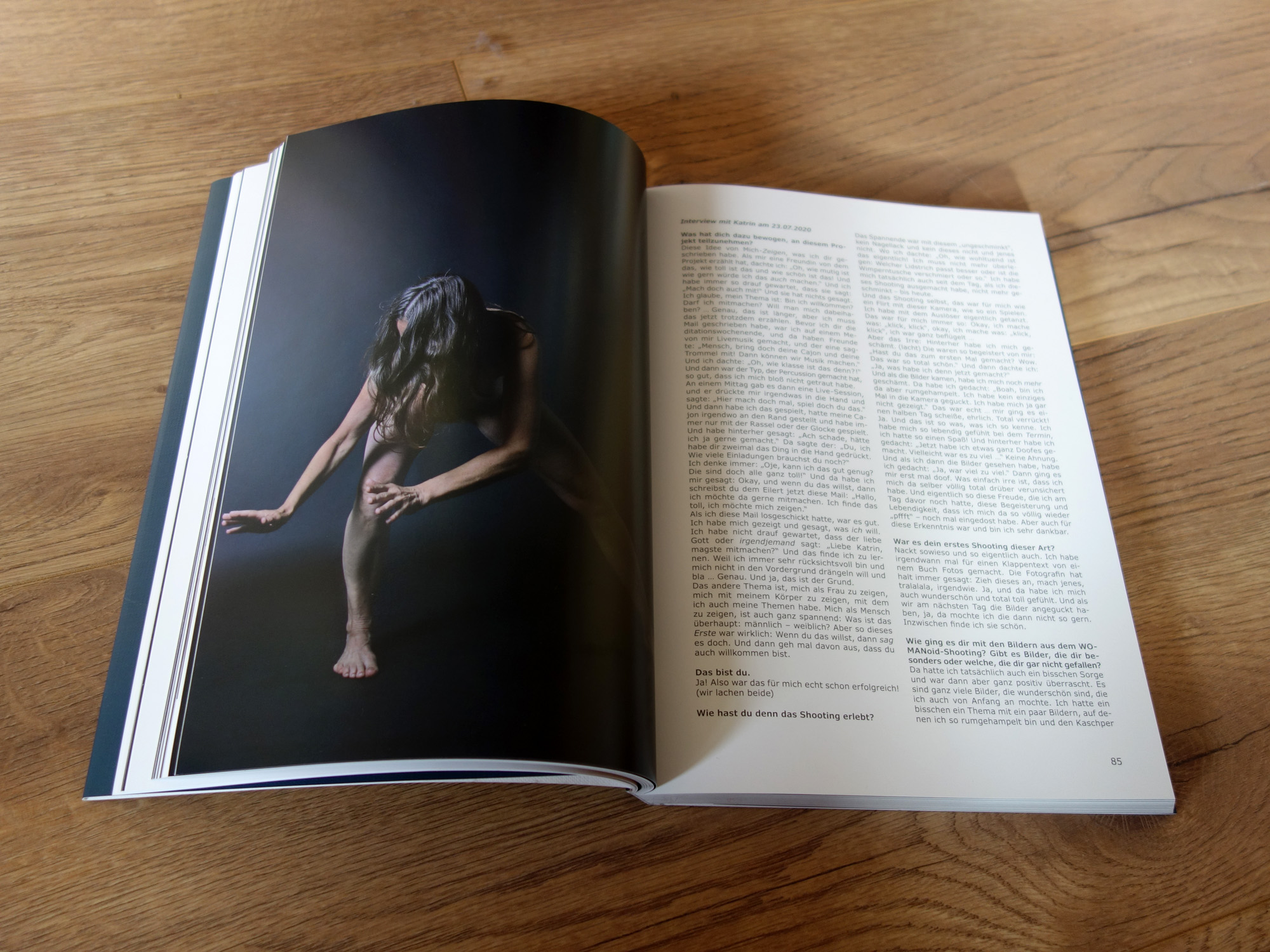 Aufgeschlagener Bildband "WOMANoid" von Eilert Bartels. Auf der linken Seite das Foto einer nackten Frau vor schwarzem Hintergrund. Sie beugt sich vor und ihre Haare verdecken einen Großteil ihres Oberkörpers.