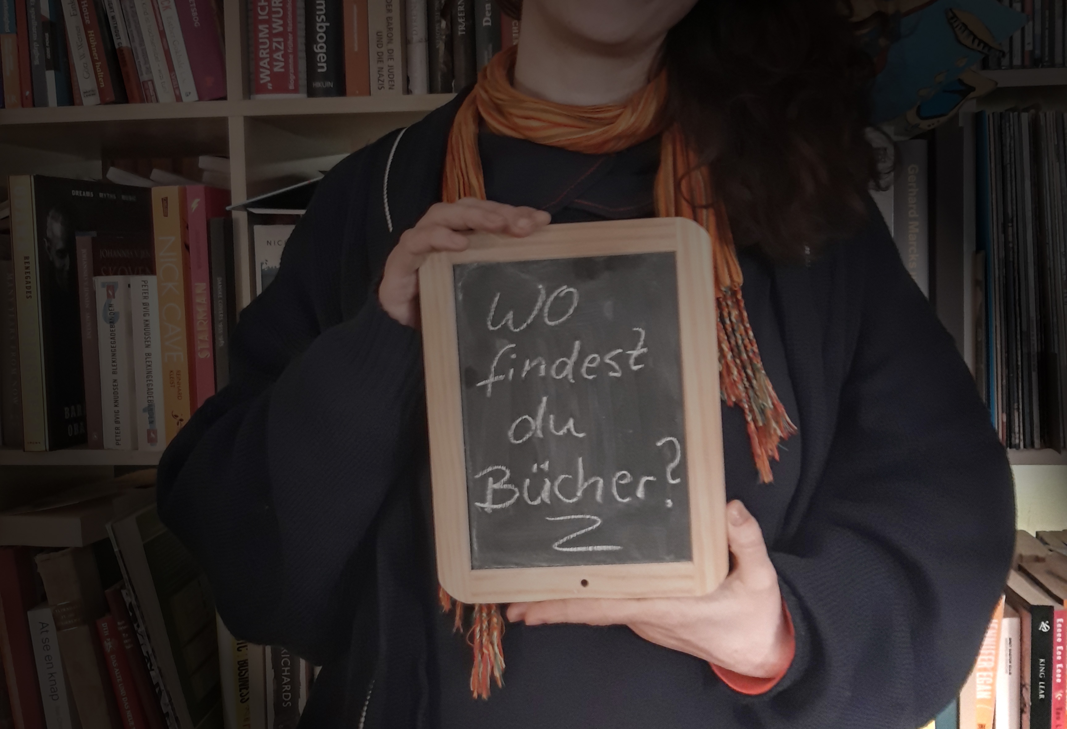 Tala T. Alsted hält eine Schiefertafel in der Hand, auf der steht: "Wo findest du Bücher?"