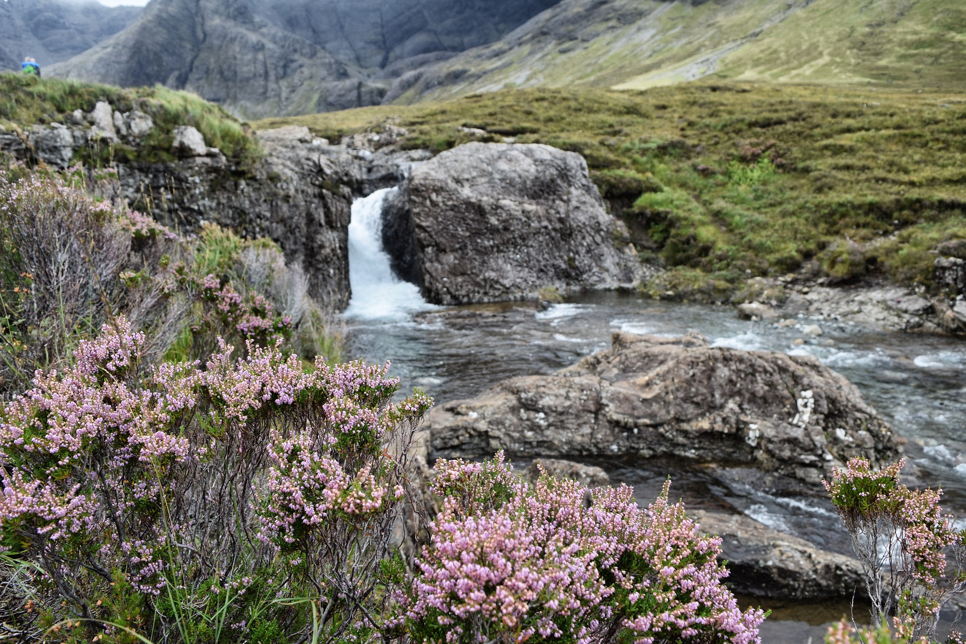 Ein kleiner Wasserfall, davor Heidekraut, im Hintergrund die schottischen Highlands (Image by Maike from Pixabay)