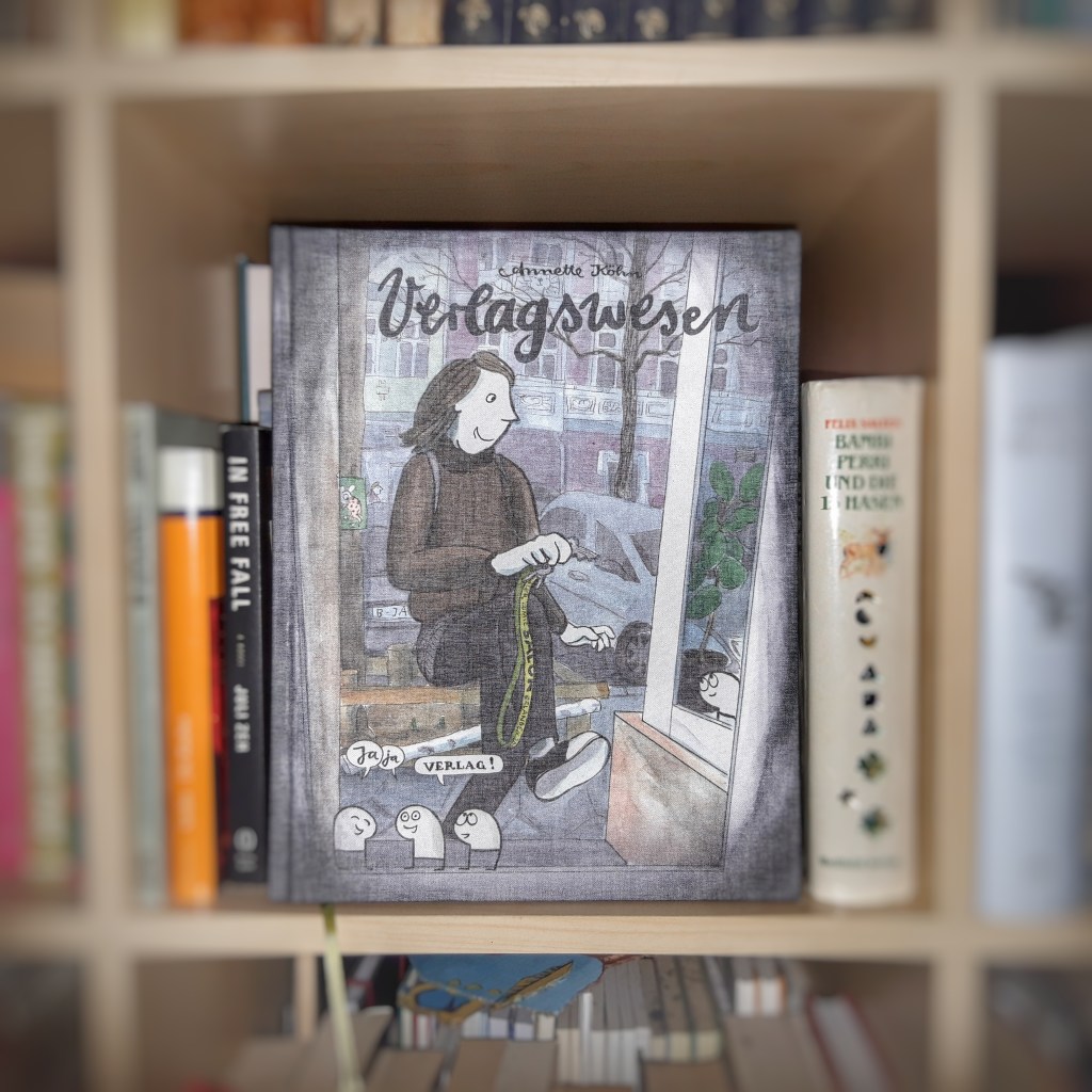 Das Comic "Verlagswesen" von Annette Köhn im Bücherregal, die umstehenden Bücher verschwommen, der Fokus auf dem Buchtitel.