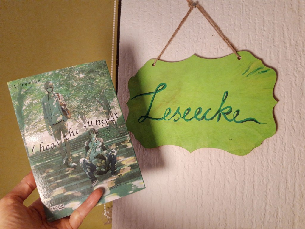 Hand hält einen Manga hoch, daneben ein handgeschriebenes Schild "Leseecke"
